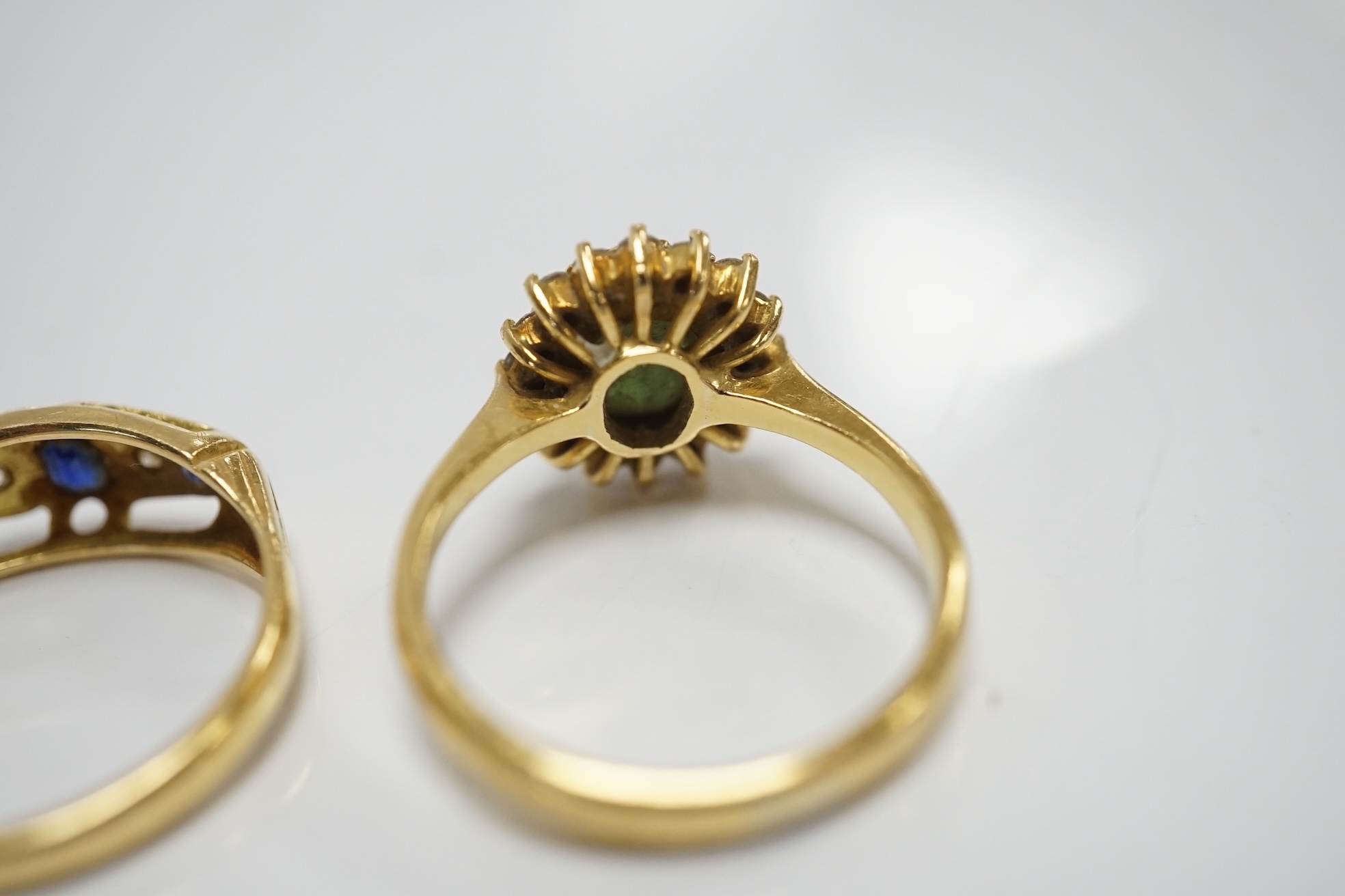 Two yellow metal and gem set rings, including a sapphire? and diamond oval cluster and a three stone sapphire and two stone diamond half hoop, gross weight 7.3 grams. Condition - poor to fair